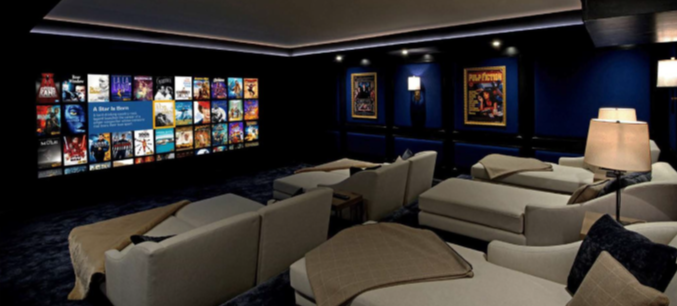 Cozy home theater with several light-colored reclining seats facing a wall-mounted screen of movie covers, dark blue walls, and framed posters.